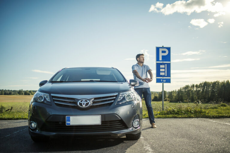 Henkilö on maantiellä ja nojaa autoonsa